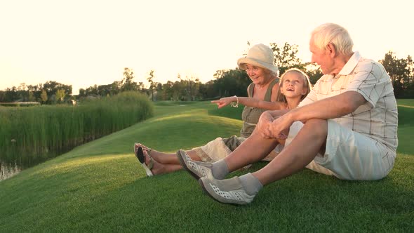 Girl and Grandparents Sitting on Grass.