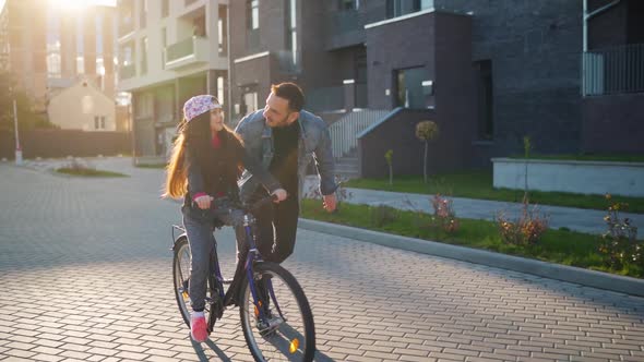 Dad Is Teaching Daughter How To Ride Bicycle at Sunset