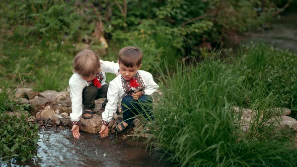 Little Ukrainian Boys in Traditional Embroidery Vyshyvanka Shirts Sitting Near River Splashes with