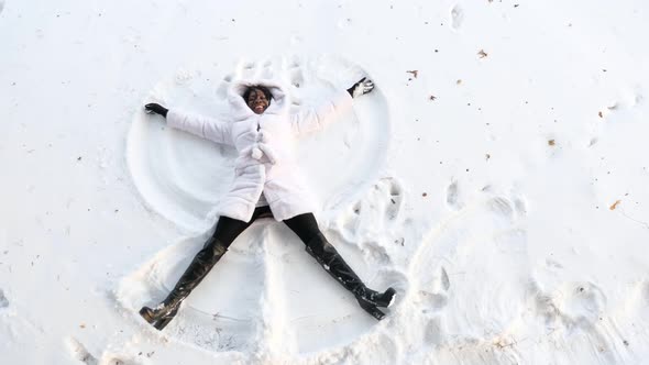 Black Girl Lies on White Forest Glade and Makes Snow Angles