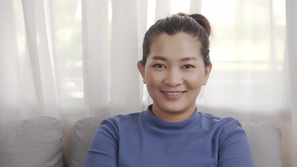 Asian woman wearing a blue shirt sitting on a sofa with smiling relax happily