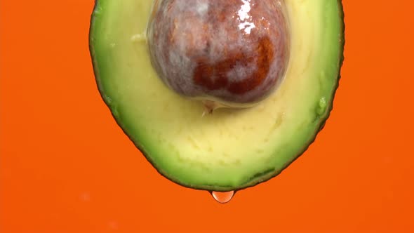 Water drops falling from avocado on orange background. Avocado slice and water splashing, drops