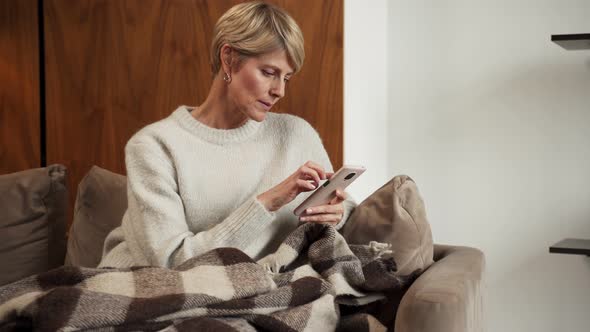 A Middleaged Woman with a Smartphone in Her Hands Sitting at Home on the Couch