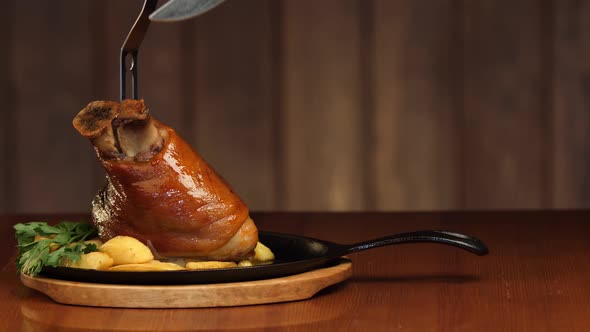 A Man's Hand Cuts a Piece of Meat From a Freshly Cooked Pork Shank with a Knife. Ready Meat Dish