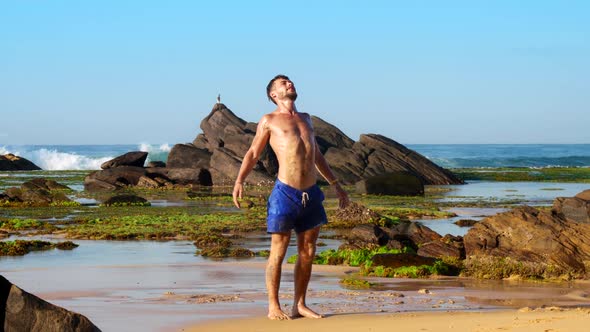 Sporty Bearded Man Stands on Wet Sand and Stretches