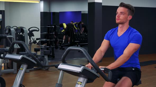 A Young Fit Man Trains on an Exercise Bike in a Gym