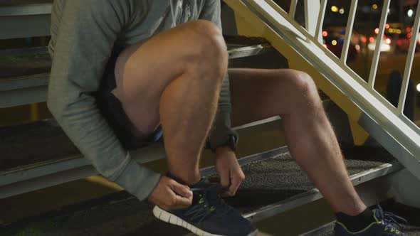 Caucasian male smiling and tying his lacet on stairs in the evening