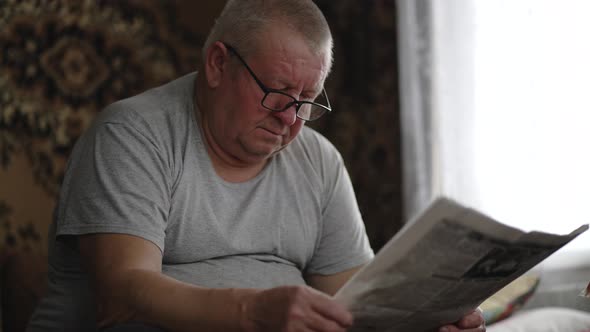 A Mature Man in Glasses Reading a Newspaper at Home