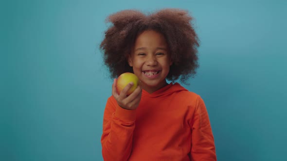 African American girl eating apple standing on blue background