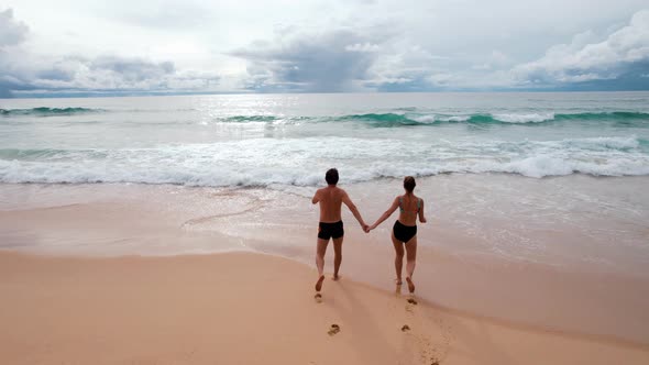 A Man and a Woman Holding Hands Go Swimming in the Big Waves of the Blue Sea