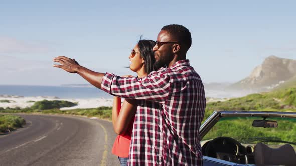 African american couple embracing each other while standing near convertible car on road