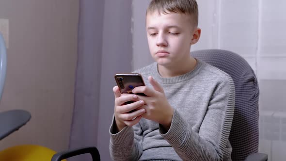 Child Sits in a Chair Holds a Smartphone in Hands Writes SMS in Chat