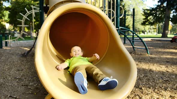 Children sliding down yellow tube slide and smiling