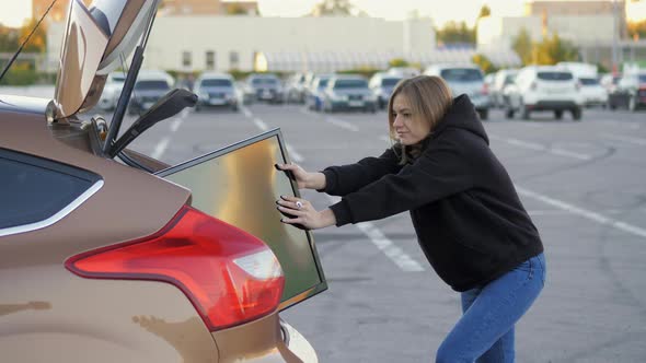 Woman Funny Trying to Put Purchased Modern Tv in Car Trunk at Supermarket Parking