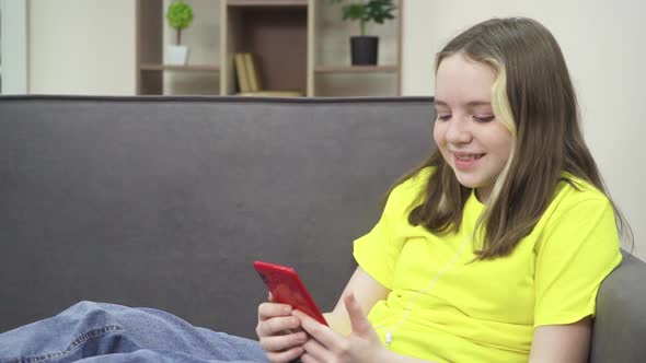 The Little Girl is Smiling and Looking at Her Phone While Sitting on the Couch