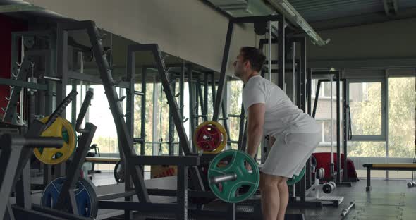 Sportsman Doing Exercise with Barbell and Flexing Muscles, Training Hands and Back at Gym