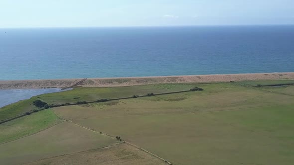 Wide aerial tracking forward over a field at the west side of Chesil Beach, Dorset. England. Bird of