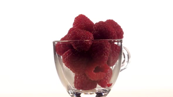 Red Raspberries in a Transparent Cup Rotates on White Background. Closeup