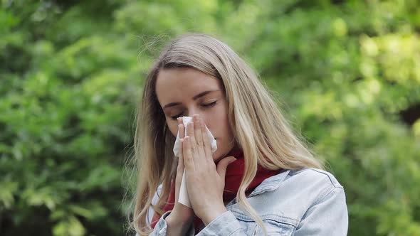 Young Woman with with Allergy Symptom Blowing Nose Standing in the Park