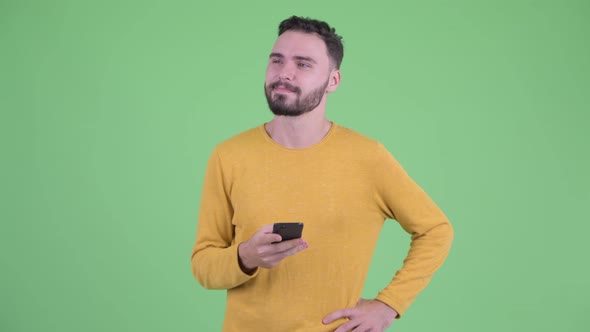 Happy Young Handsome Bearded Man Thinking While Using Phone