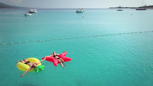 Aerial view of man and woman floating by string buoy on inflatable mattresses.