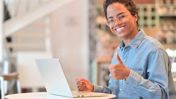 African Woman with Laptop Showing Thumbs Up Sign in Cafe 