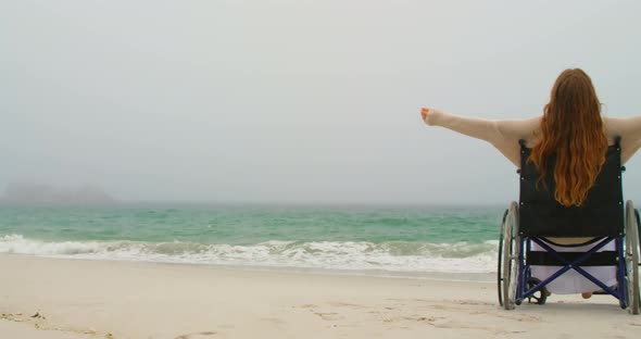 Side view of young Caucasian woman sitting with arms outstretched on wheelchair at beach 4kouple hav