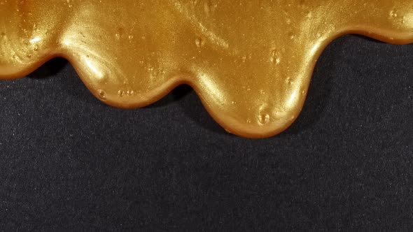 Golden Liquid Gel with Micro Bubbles As It Slowly Slides Down on the Black Surface