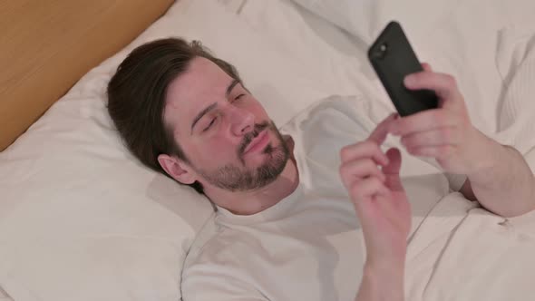 Casual Young Man Using Smartphone While Sleeping in Bed