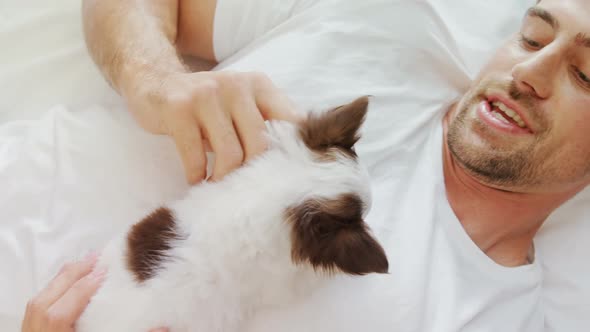 Happy young man lying on bed stroking his puppy in the bedroom 4K 4k