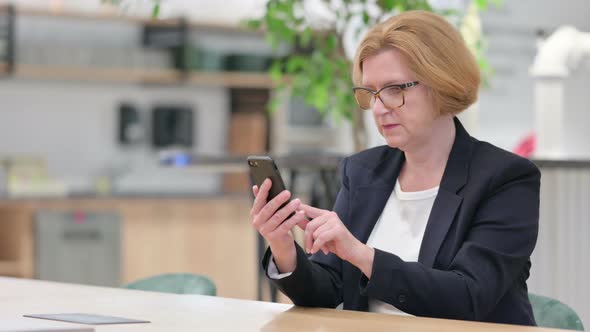 Old Businesswoman with Success on Smartphone in Office 