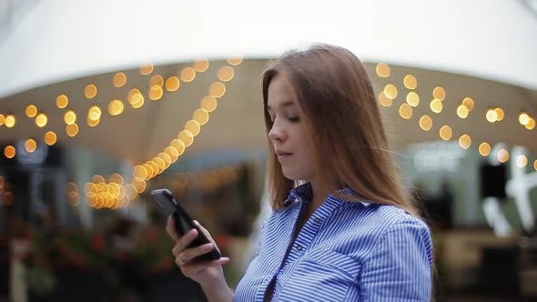 Close-up View of Beautiful Young Girl in Striped Shirt Watching Video on Smartphone Then Looking at