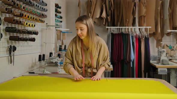 Close up of female designer unwinding a big yellow roll of fabric tissue on table at design studio