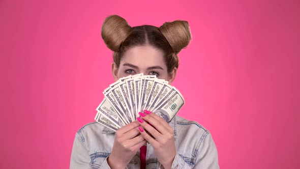 Girl Holds Paper Bills and Winks. Pink Background. Slow Motion