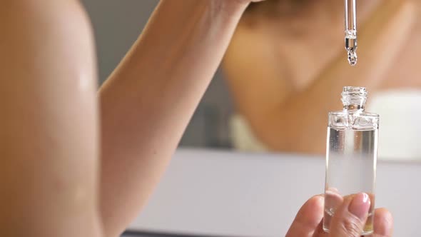 Female Hand Holds a Cosmetic Serum in a Glass Bottle with a Pipette