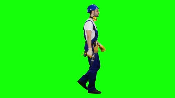 Man Working From a Construction Site Comes with a Drill in His Hands. Green Screen. Side View