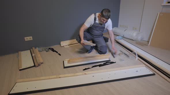 A Builder in a Work Overalls is Assembling a Bed in a New Apartment