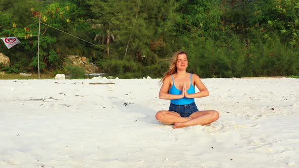 Young woman concentrating on Yoga exercises sitting on white sand of exotic beach in front with sea