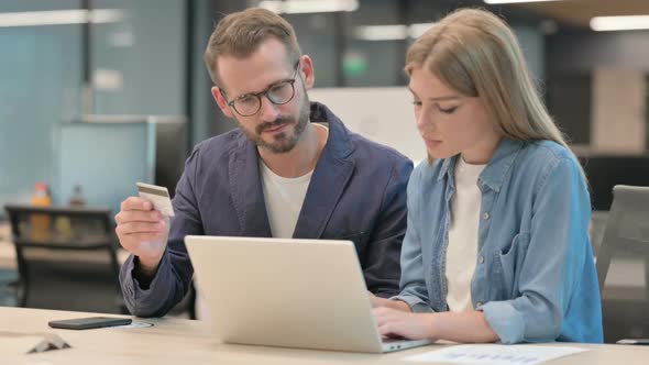 Male and Female Professionals Talking While Making Online Payment on Laptop