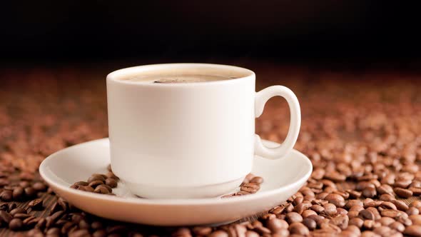 Steam Rises From a Mug of Hot Coffee Against a Background of Roasted Coffee Beans