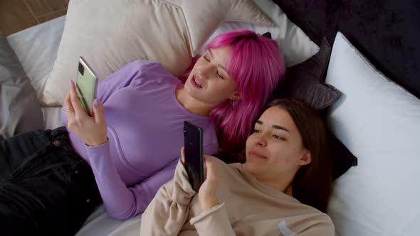 Joyful Attractive Female Friends with Smartphones Enjoying Leisure on Bed