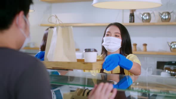 Attractive asian female cafe worker  giving takeaway food bag to customer