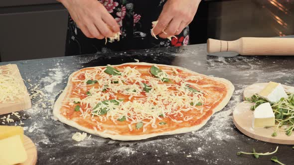 Female chef adding cheese on pizza base, preparing italian pizza margherita.