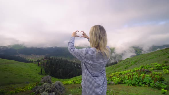 Young girl makes her fingers and hands heart in mountains.