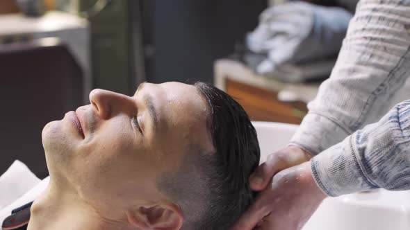 a Hairdresser Washes the Hair of a Brunette Man in a Barbershop