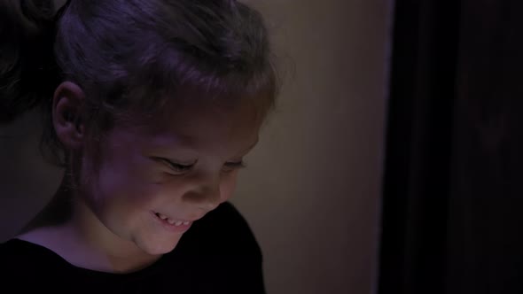 Little Girl Sitting on the Floor and Playing Tablet or Smartphone in Social Internet in Dark Blue