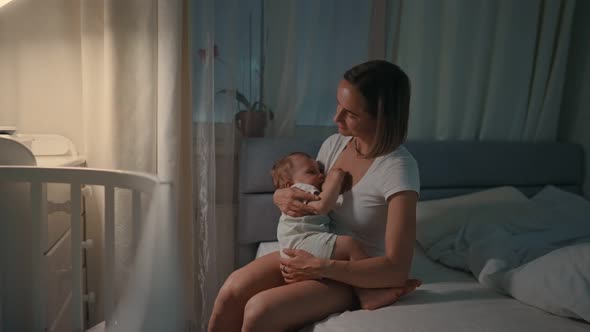 Young Beautiful Mother Breastfeeding Her Newborn Baby Boy at Night Dim Light