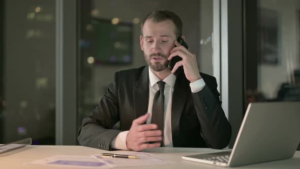 Ambitious Businessman Talking on Cellphone in Office at Night