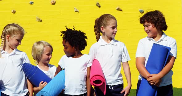 School kids holding yoga mat and interacting with each other