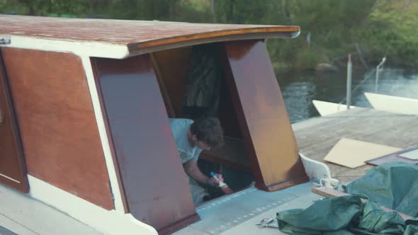 Young man painting wooden boat wheelhouse cabin